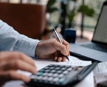 Free A person calculating finances with a calculator and pen on a desk indoors. Stock Photo