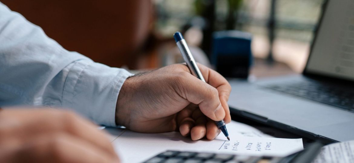 Free A person calculating finances with a calculator and pen on a desk indoors. Stock Photo