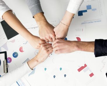 Free Colleagues celebrate success with a fist bump over financial charts depicting teamwork and unity. Stock Photo