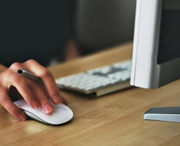 Free A hand using a wireless mouse at a modern desk setup with a computer and keyboard. Stock Photo