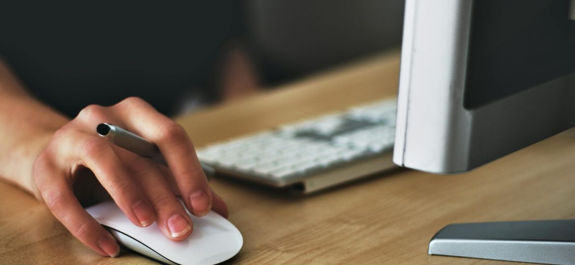 Free A hand using a wireless mouse at a modern desk setup with a computer and keyboard. Stock Photo