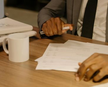 Free Close-up of a businessman holding and reviewing documents on a wooden desk. Stock Photo