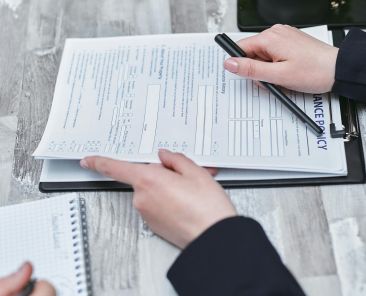 Free Close-up of hands analyzing insurance policy paperwork with pen on table. Stock Photo